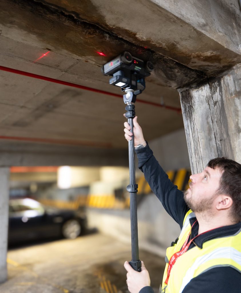 Trace surveyor scanning a spalled concrete beam soffit from below